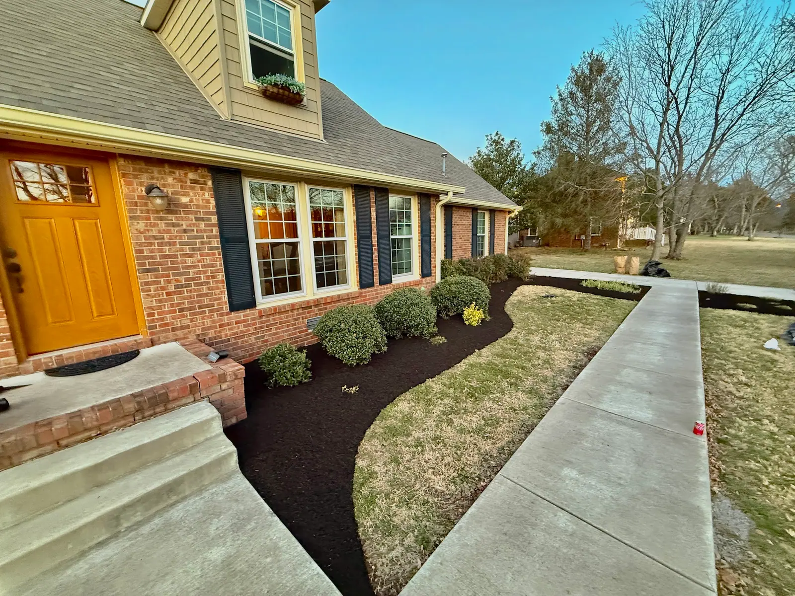 Mulch bed along a walkway and a brick house with an orange door