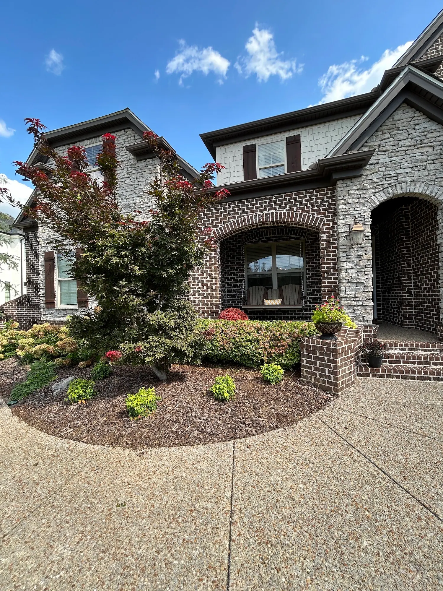 Flowering shrubs and a mulch bed at a stone and brick house entrance