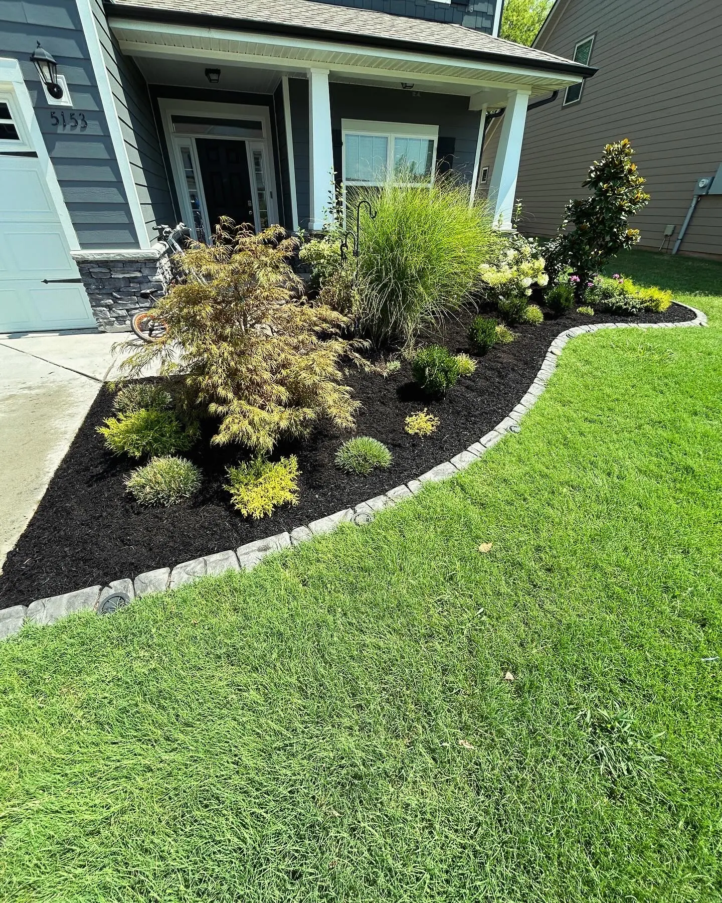 Stone-edged mulch bed with ornamental grasses and shrubs by a house
